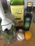 Trusty hand blender in blender pot full of greens, with gartlic, lomon juice, balsamic and olive oil standing by